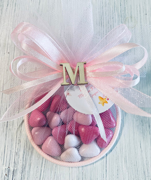 bomboniera portaconfetti a forma di cerchio o anello in metallo rosa completo di confetti a forma di cuoricini al cioccolato fondente sfumati, nastrini rosa abbinati, bigliettino stampato e personalizzato con iniziale del nome in legno. Portaconfetti come bomboniera di nascita, battesimo.